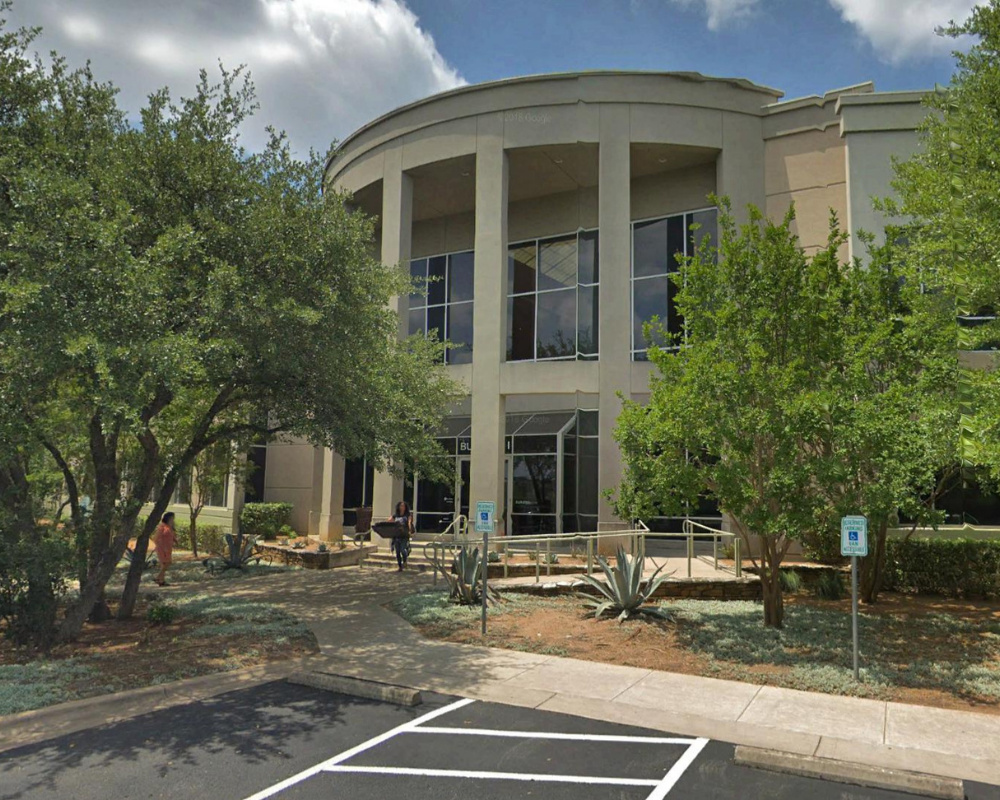 Office building with columns and glass entrance surrounded by trees and landscaping