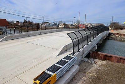 Concrete roadway bridge with protective side fencing spanning a narrow waterway in a residential area