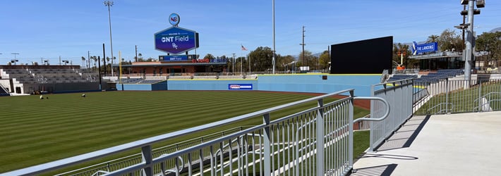 View from stadium seating showing baseball field, outfield scoreboard, and surrounding stands under clear sky