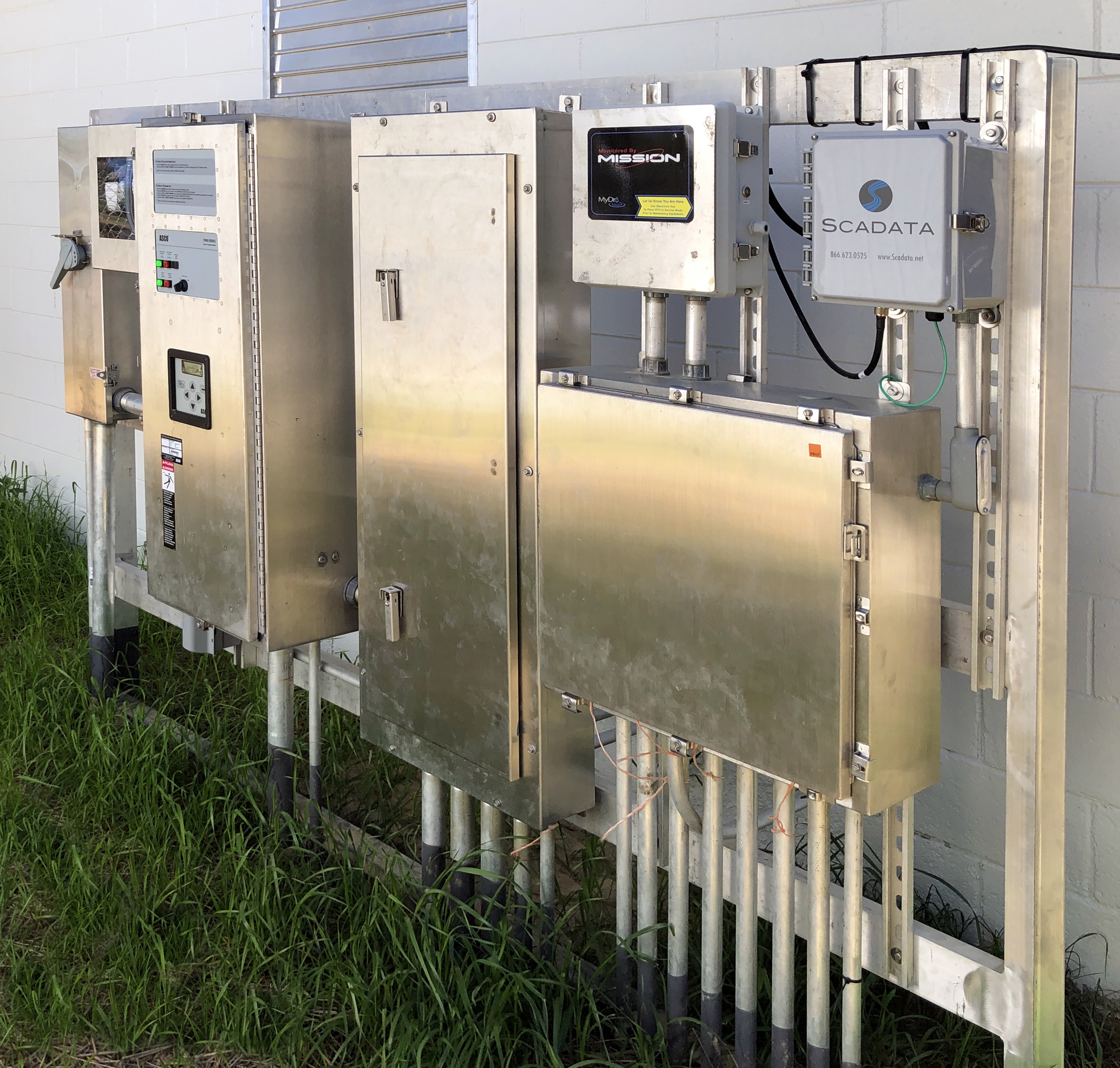 Stainless steel control panels and SCADA monitoring boxes mounted on pipes outside a facility