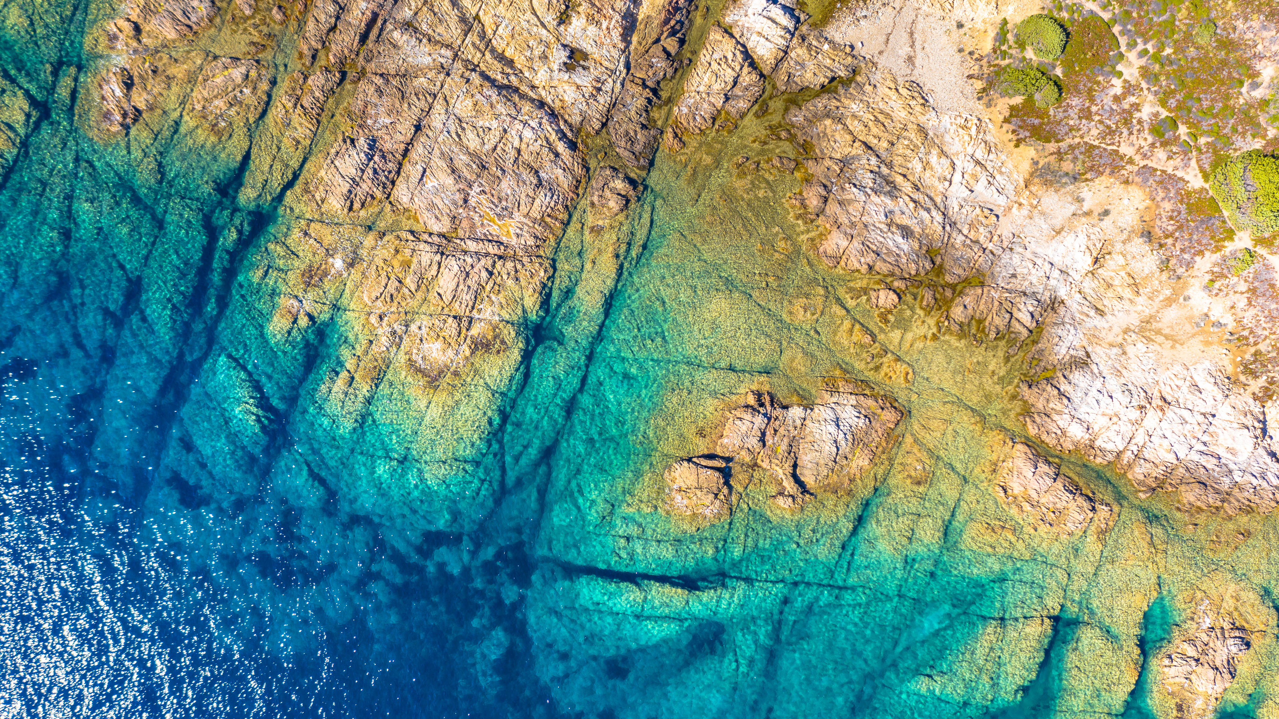 Aerial view of rocky shoreline with clear turquoise water and submerged rock formations